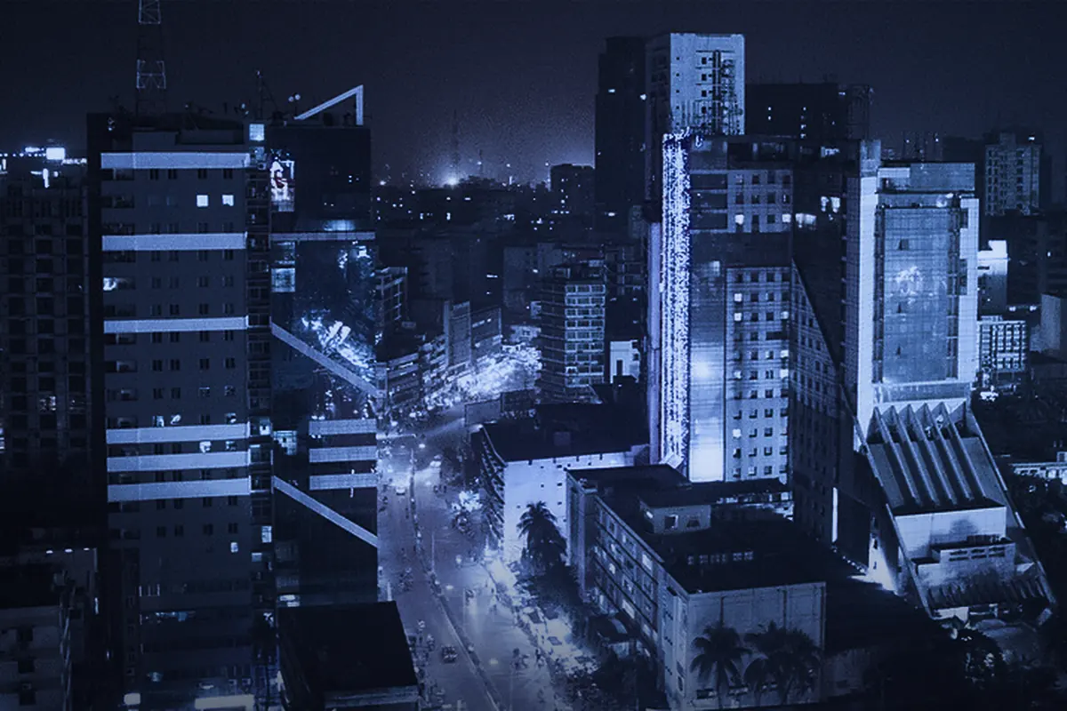 Dhaka after dark from above: lit mid-rise towers along a busy road.